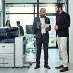 Zwei Männer in einem Büro diskutieren etwas auf einem Tablet neben einem Farbmultifunktionsdrucker der Xerox® AltaLink® C8200-Serie Xerox Multifunktionsdrucker mi KI-Technologie. AltaLink B8245, AltaLink B8255, AltaLink B8270, AltaLink C8235, AltaLink C8245, AltaLink C8255 AltaLink C8270.
