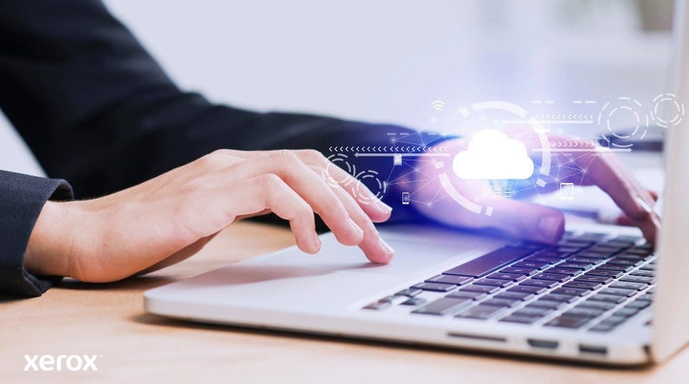 Xerox® Workplace Cloud und Suite: Cloud-Konnektivität Zu sehen sind die Hände einer Person, die auf einer Laptoptastatur tippt. Über das Bild sind ein leuchtendes Wolkensymbol und Netzwerkverbindungen gelegt, die Cloud-Konnektivität und digitale Arbeitsabläufe symbolisieren.